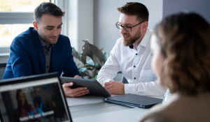 Drei Vertriebsmitarbeiter sitzen mit Laptop und Tablet an einem Konferenztisch und besprechen Vertriebsthemen.