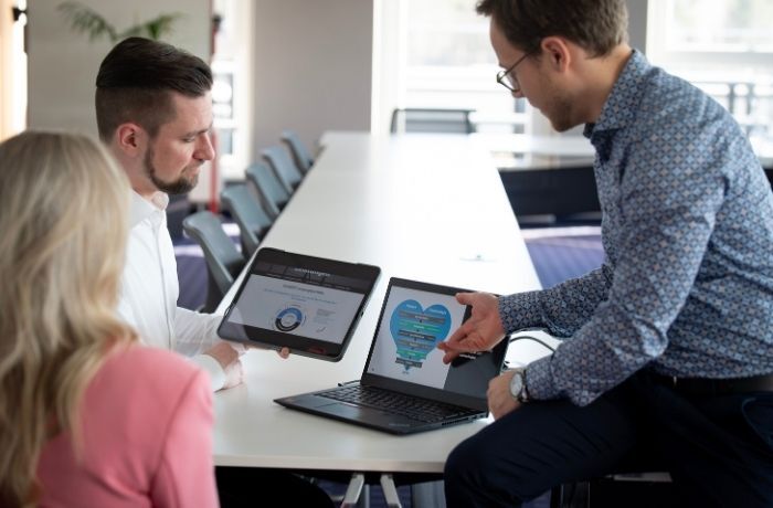 Ein Sales Manager zeigt zwei Kunden von SUXXEED etwas am Laptop im Meeting Büro